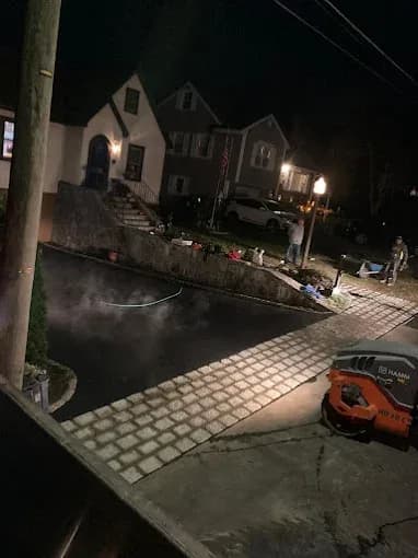 Nighttime residential asphalt paving with steam rising from fresh pavement