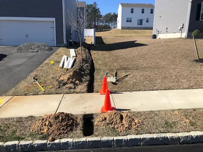 Utility trench cut through a lawn and under a sidewalk with safety cones