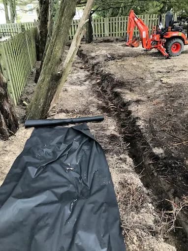 Excavated drainage trench with landscape fabric and compact backhoe on site