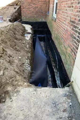 Worker compacting gravel base with a plate compactor beside PVC pipe