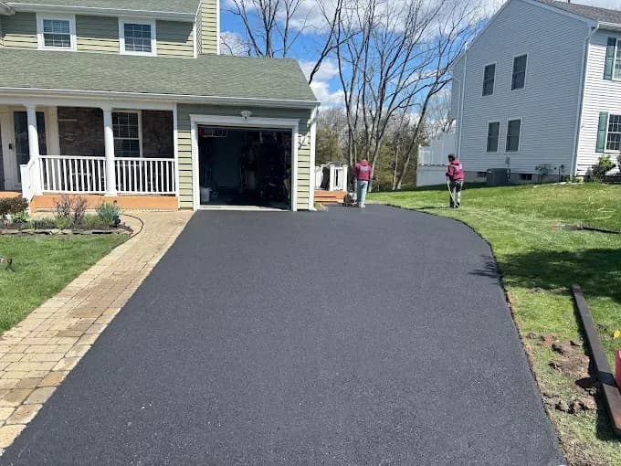 New asphalt driveway with paver border and caution tape at a white home