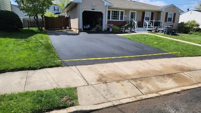 Fresh asphalt driveway with caution tape in front of a ranch-style home